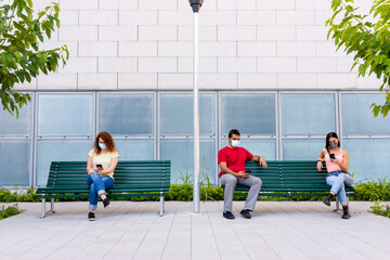 young people sit on different benches respecting the social distancing imposed by the rules of prevention during coronavirus outbreak, new normal with millennials addicted to smart phones