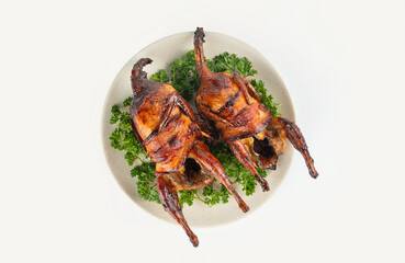 Baked quail with herbs on a white plate. View from above.