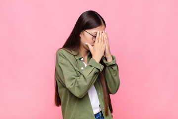 asian young woman covering eyes with hands with a sad, frustrated look of despair, crying, side view