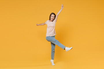 Fototapeta na wymiar Full length portrait of funny surprised cheerful young woman 20s in pastel pink casual t-shirt posing dancing rising spreading hands and legs looking camera isolated on yellow color background studio.