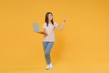 Full length portrait of smiling young brunette woman 20s in pastel pink casual t-shirt hold laptop...