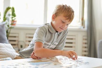 Portrait of smiling teenage boy playing with puzzles alone while enjoying leisure time indoors, copy space