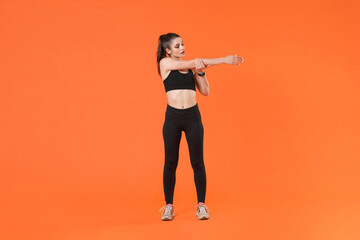 Fototapeta na wymiar Full length portrait of attractive young fitness sporty woman in black sportswear posing training working out doing stretching exercising looking aside isolated on orange color wall background studio.