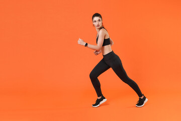 Fototapeta na wymiar Full length side view portrait of beautiful strong young fitness sporty woman 20s wearing black sportswear training working out running looking aside isolated on orange color wall background studio.