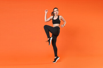 Fototapeta na wymiar Full length side view portrait beautiful young fitness sporty woman in black sportswear posing training jumping dancing doing cardio exercising rising hands legs isolated on orange background studio.