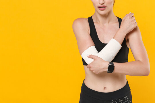 Cropped image of young fitness sporty woman 20s wearing black sportswear posing training get injured touching arm elbow with elastic bandage isolated on bright yellow color background studio portrait.