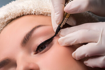 Permanent eye makeup close up shot. Cosmetologist applying tattooing of eyes. Makeup eyeliner procedure - obrazy, fototapety, plakaty