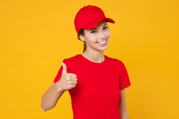 Delivery employee woman in red cap blank t-shirt uniform workwear work courier in service during quarantine coronavirus covid-19 virus, showing thumbs up isolated on yellow background studio portrait.