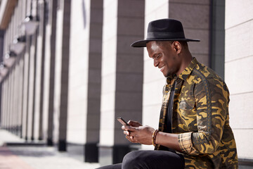 good-looking black male use smartphone while he is walking outdoors, stylish guy chatting with girlfriend