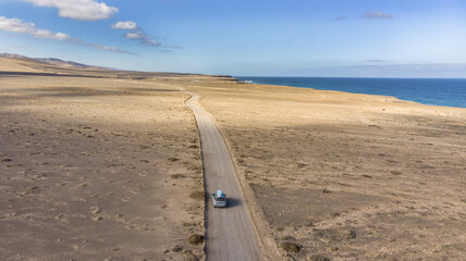 Aerial view of a car traveling on a road with a surfboard on the roof. Leisure trip in the summer. Tourists traveling in search of a beach where they can surf