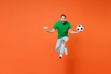 Fototapeta na wymiar Full length portrait screaming man football fan in green t-shirt cheer up support favorite team with soccer ball hold bowl of chips jumping isolated on orange background. People sport leisure concept.