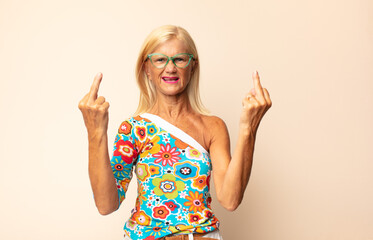middle age woman feeling provocative, aggressive and obscene, flipping the middle finger, with a...