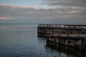Fototapeta premium old large wooden pier stands on shore of lake, seaside in the evening at sunset in water reflected in ripples