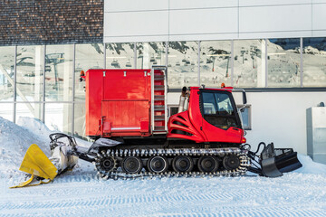 Red modern snowcat ratrack with snowplow snow grooming machine preparing ski slope piste hill at...