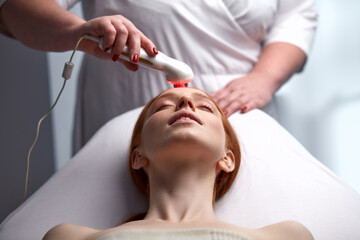 Fototapeta premium adorable young woman enjoying electric microcurrent massage by cosmetologist, hardware modern facelifting procedure in beauty salon. skin care concept, healthy lifestyle