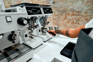 Young attractive woman barista prepares coffee for client on espresso machine in coffee shop.