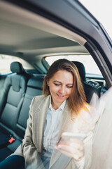 Business lady looking on phone and typing text. Businesswoman using smartphone while traveling by car on the backseat.
