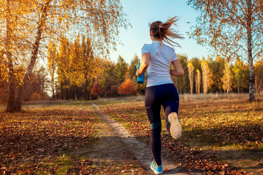 Runner training in autumn park. Young woman running at sunset in sportive clothes. Active lifestyle. Back view