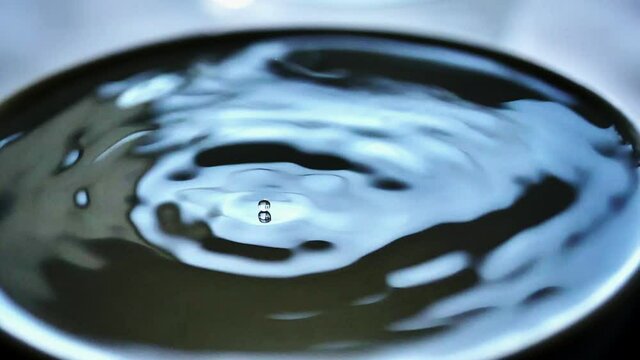 Water droplet lands in slow motion on top of waves bounces back and starts surfing