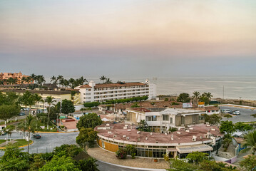 Fototapeta na wymiar Puerto Vallarta, Mexico - April 25, 2008: Morning yellow-orange light over ocean with circular port authority offices up front on harbor. Other buildings around with green foliage.