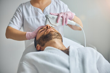 Obraz na płótnie Canvas Female beautician treating male skin with laser device