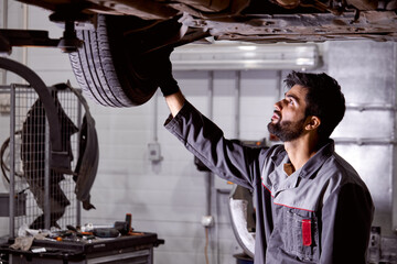 young caucasian auto mechanic in uniform is examining car wheels in auto service. male is concentrated on work