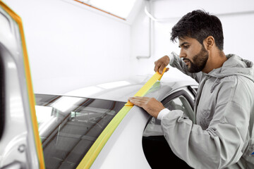 mechanic caucasian man with yellow paper tape plasters car for polishing it, paint and varnish,...