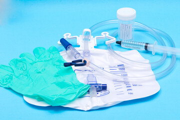 Sterile urinary drainage bag, 10 ml syringe pre-filled with sterile water and specimen container with lid and label. Isolated on blue background.