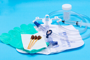 Sterile Urinary Drainage Bag with Anti-Reflux Tower, green vinyl sterile gloves and Povidone Iodine Swabsticks  isolated on blue background.