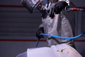 close-up photo of male hands spraying varnish at car, wearing gloves and uniform, at work place