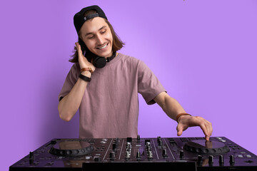 positive male DJ playing music on purple background, caucasian long haired man in casual wear...