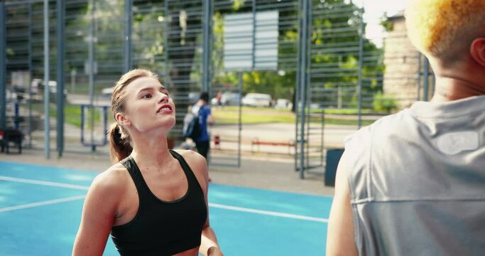Close up portrait of multi-ethnic male and female practicing streetball outdoors. Beautiful Caucasian girl and African American man basketball players playing on local court. Girl throwing ball.