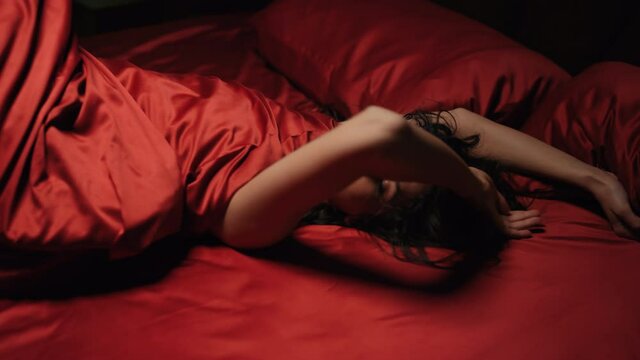 Graceful woman posing red silk bed. Bare female person looking camera bedroom.