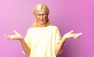 middle age woman shrugging with a dumb, crazy, confused, puzzled expression, feeling annoyed and...