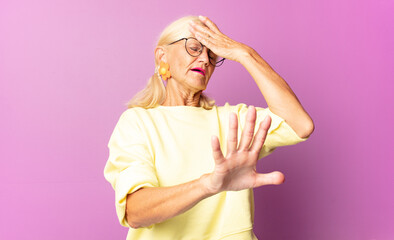 middle age woman covering face with hand and putting other hand up front to stop camera, refusing...