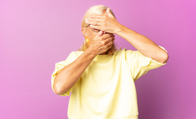 middle age woman covering face with both hands saying no to the camera! refusing pictures or...