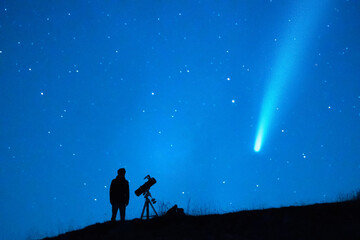 Astronomy lover with a telescope observing a comet in the blue starry sky at night. Silhouette of a person observing the immensity of the universe and the stars. Trace of a comet or a shooting star.