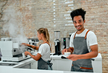 Beautiful caucasian woman and attractive African male baristas are making coffee in the coffee shop.