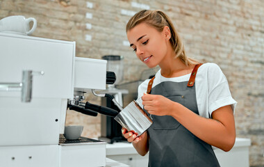 Young attractive woman barista prepares coffee in a coffee shop.
