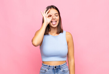young pretty woman smiling happily with funny face, joking and looking through peephole, spying on...