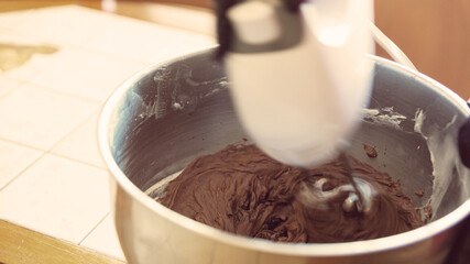 Chocolate butter cream in a metal bowl. Beating cream cake. Mixer whisk in cream
