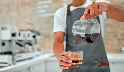 Attractive African male professional barista in apron prepares coffee in the cafeteria.