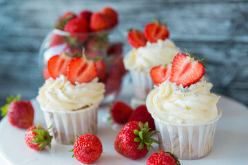 Delicious cupcakes with white cream decorated with ripe strawberries on a gray blue background.