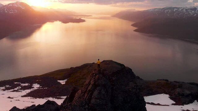 Man on Mountain with Snow Midnight Sun Fjord Ocean Aerial Drone Footage Norway