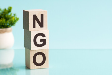 Word NGO - Non-governmental organization - on a wooden cubes on a blue background