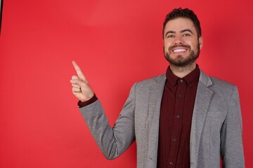 Young caucasian businessman wearing casual clothes standing over isolated red background looking indicating fingers hands side empty space advising novelt
