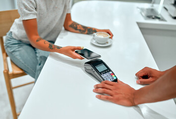 Female customer making payment through mobile phone at counter in cafe with young man. Barista holding credit card reading machine in front of female costumer with cell phone.