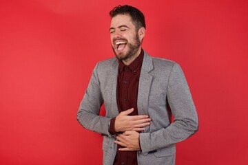Young caucasian businessman wearing casual clothes standing over isolated red background smiling and laughing hard out loud because funny crazy joke with hands on body.