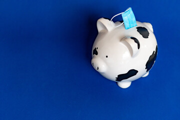 piggy bank on blue background saving a face mask in coronavirus times covid-19