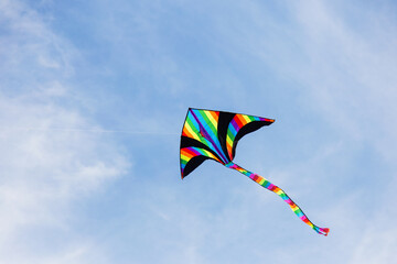 Colorful kite flying in the cloudy sky. Bright multicolored kite on a background of white clouds and blue sky